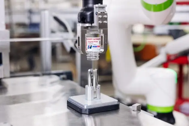 A robot removes containers from the magnetically floating XPlanar movers when printing is complete.